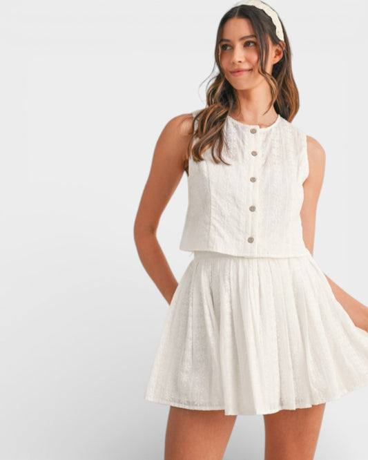 Woman wearing a white sleeveless top and skirt set on a plain background