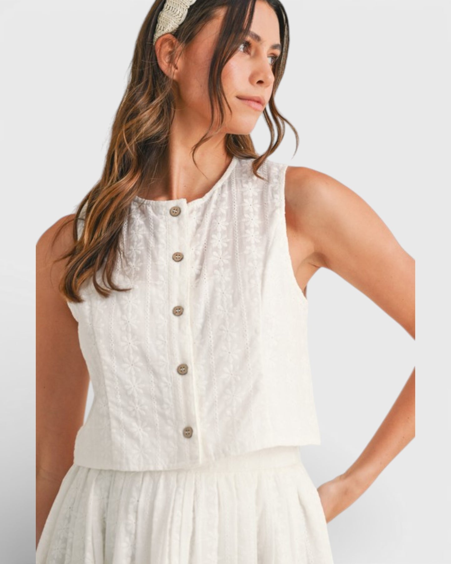 Woman wearing a white sleeveless top with buttons on a plain background