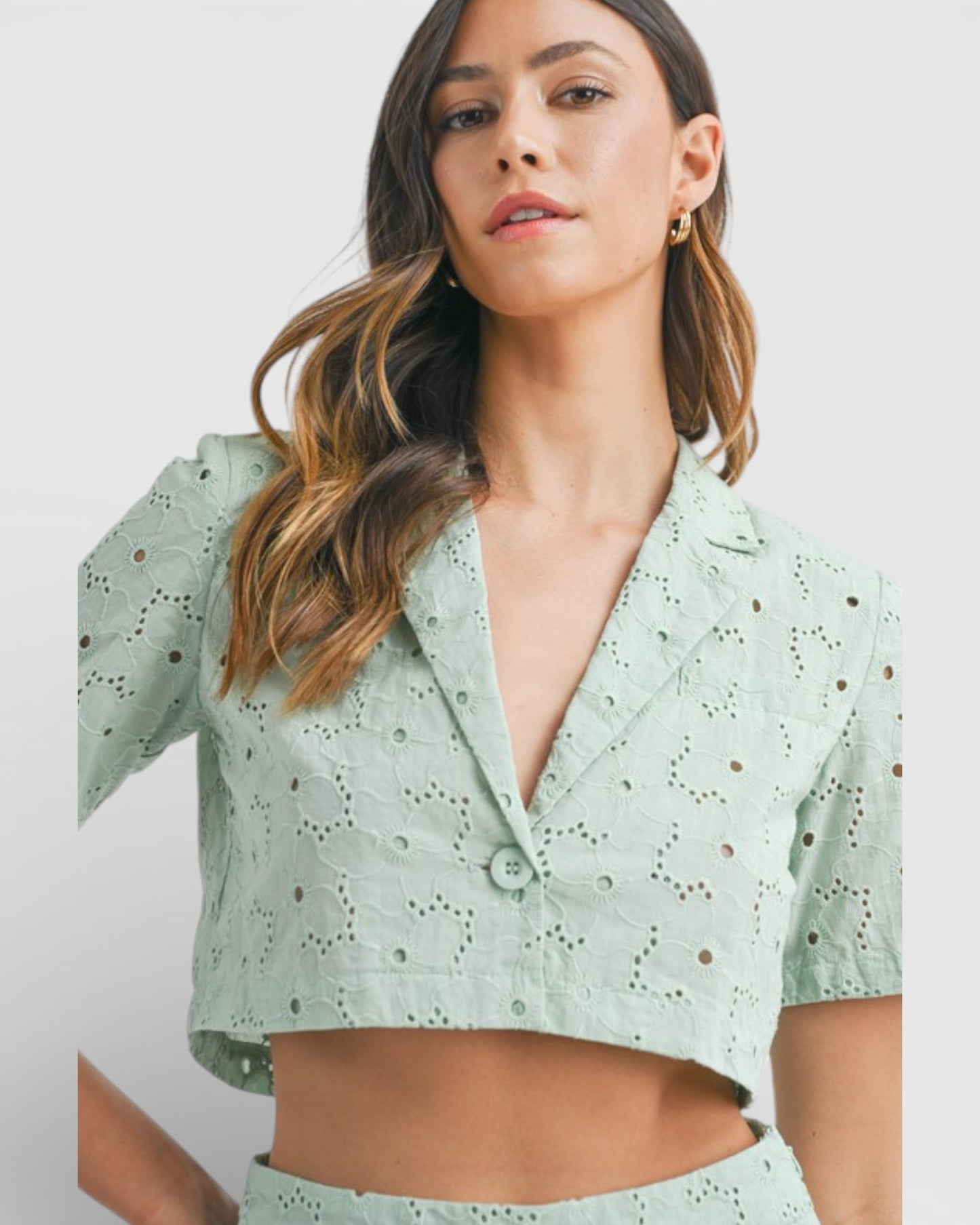 Woman wearing a light green blouse with a subtle pattern on a plain background