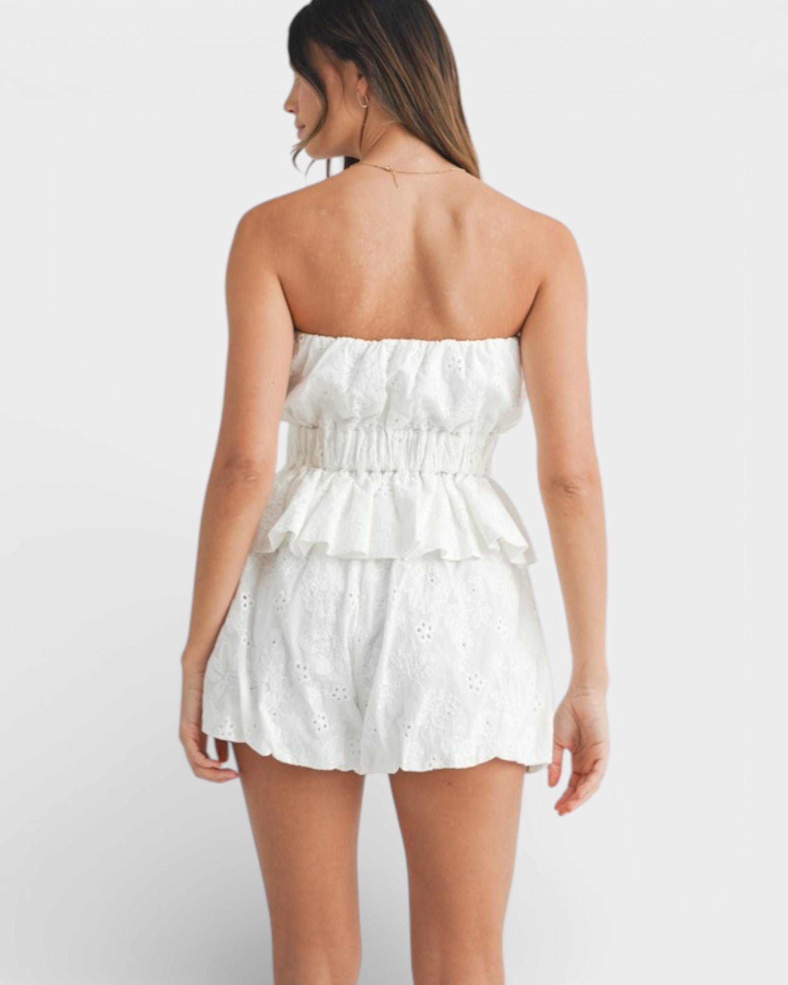Woman wearing a white strapless romper on a plain background