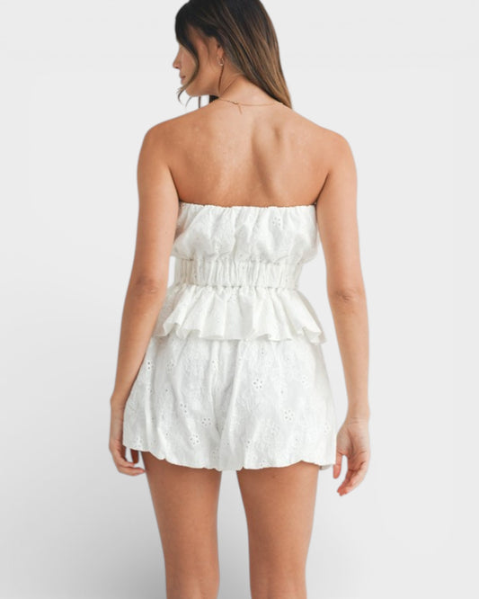 Woman wearing a white strapless romper on a plain background
