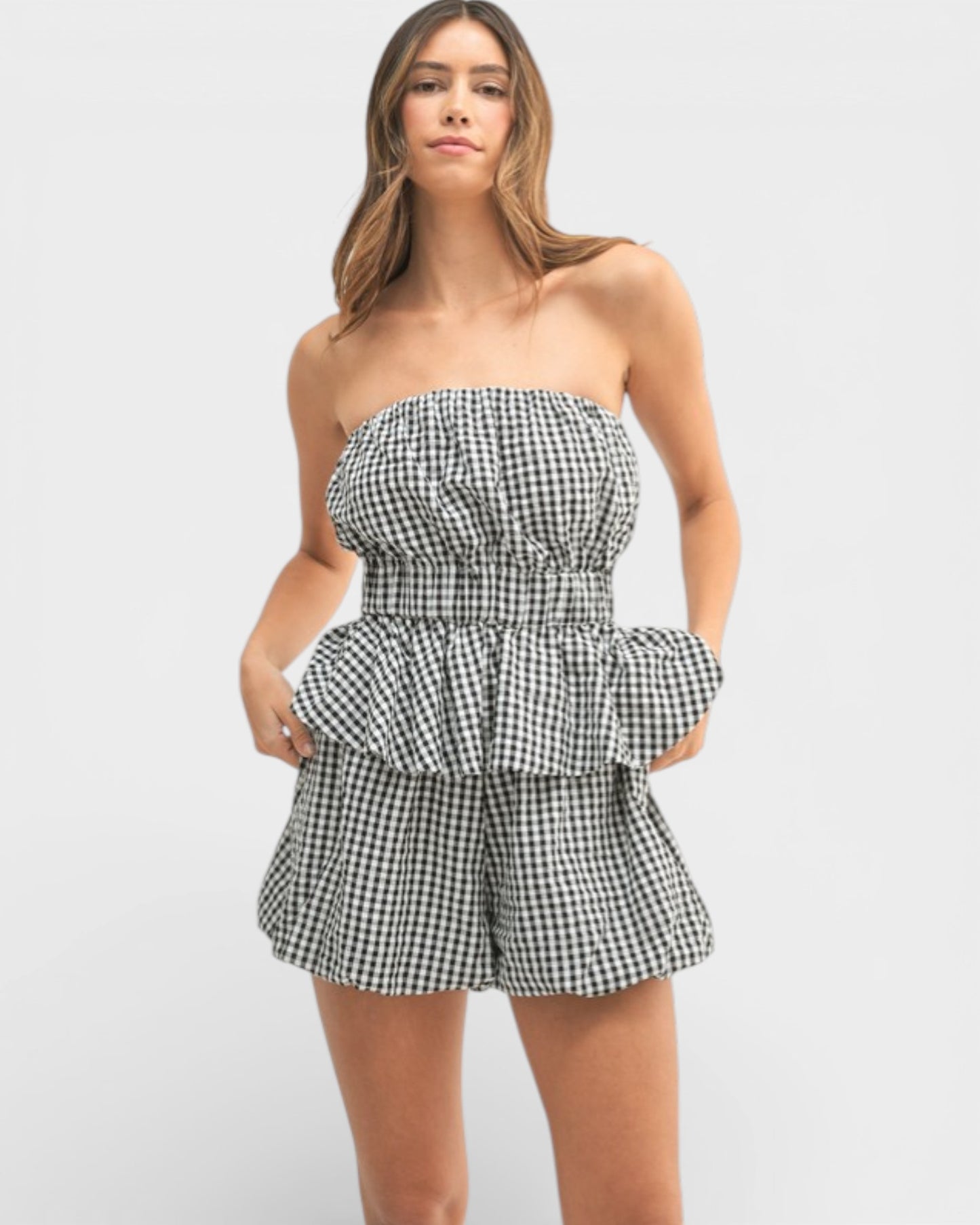 Woman wearing a black and white checkered strapless romper on a light gray background
