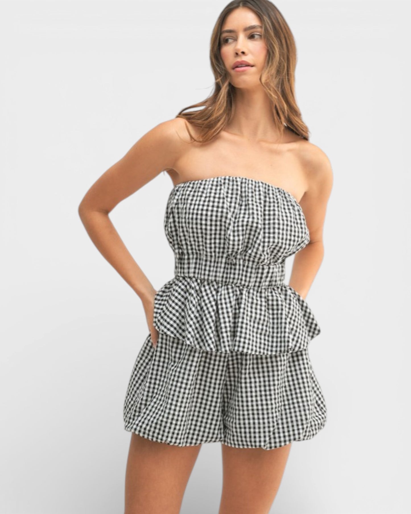 Woman wearing a strapless gingham romper on a white background