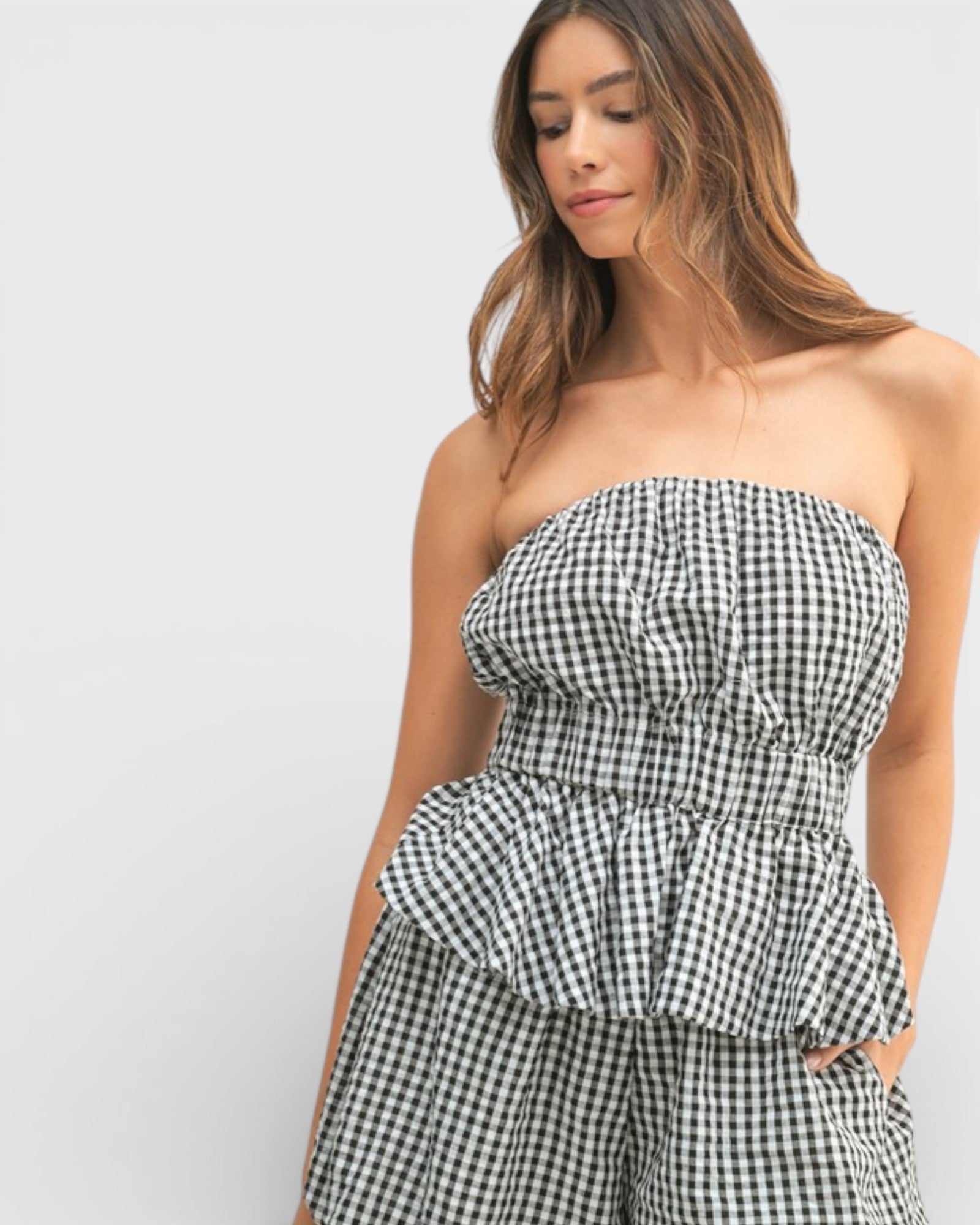 Woman wearing a black and white checkered strapless top and shorts on a light gray background