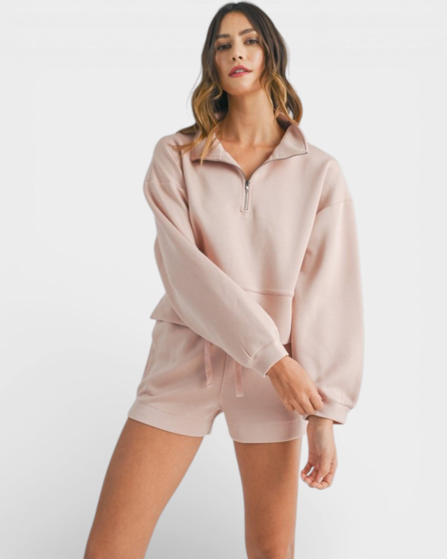 Woman wearing a light pink hoodie and shorts set on a white background