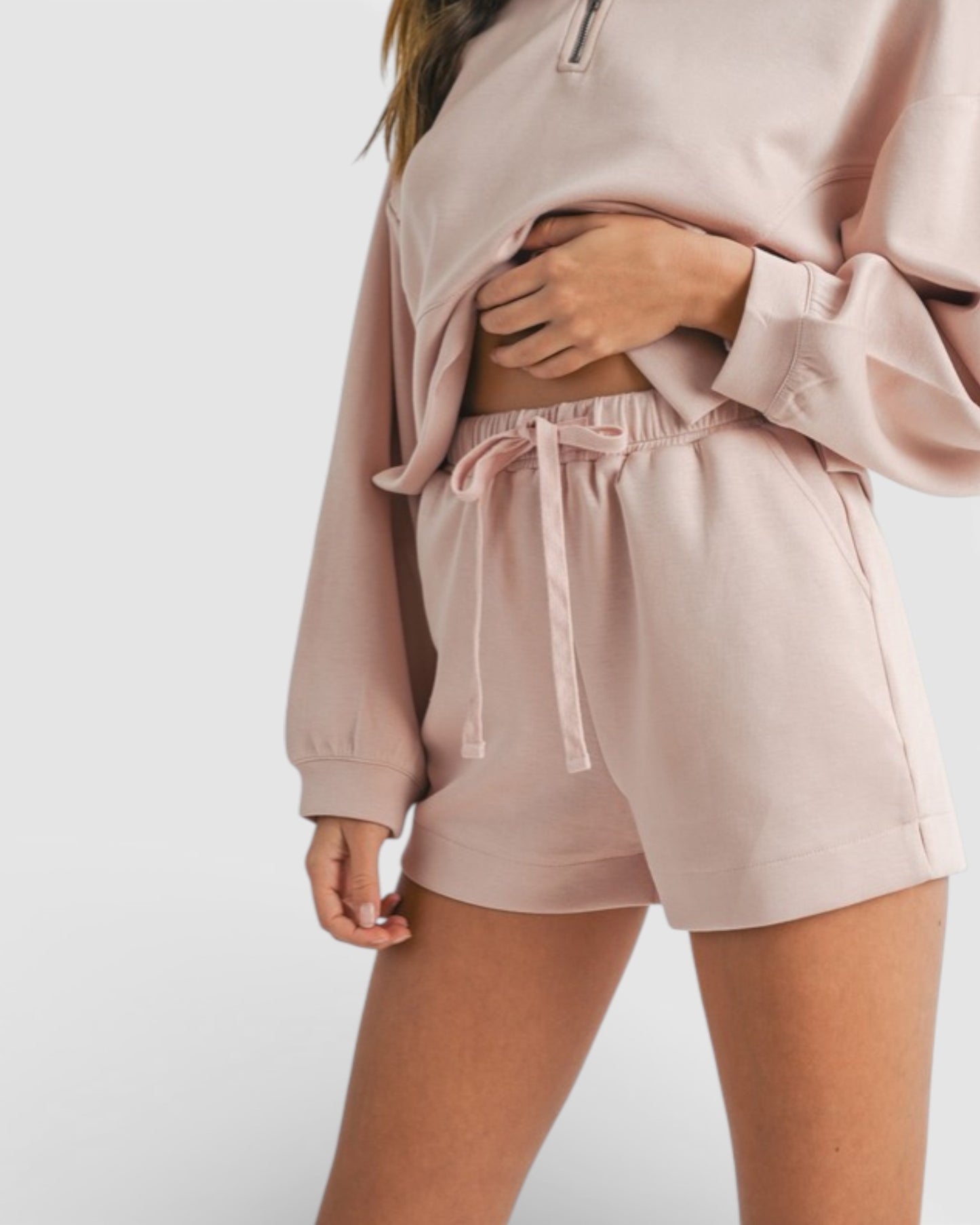 Person wearing a matching pink sweatshirt and shorts set on a white background