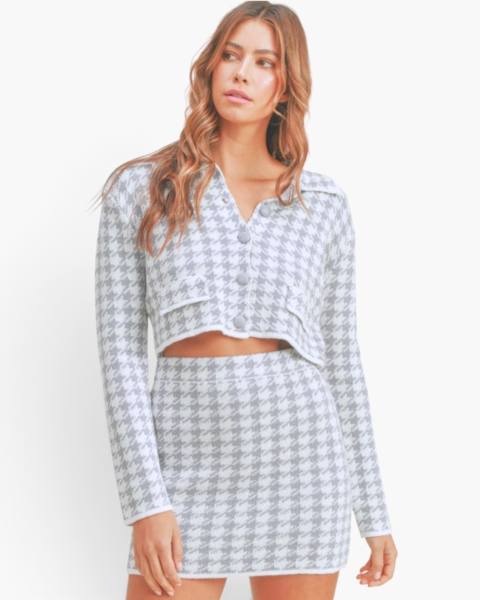A woman modeling a matching two-piece knit set featuring a long-sleeve cropped button-front top and a high-waisted mini skirt, both in a light gray and white houndstooth pattern.
