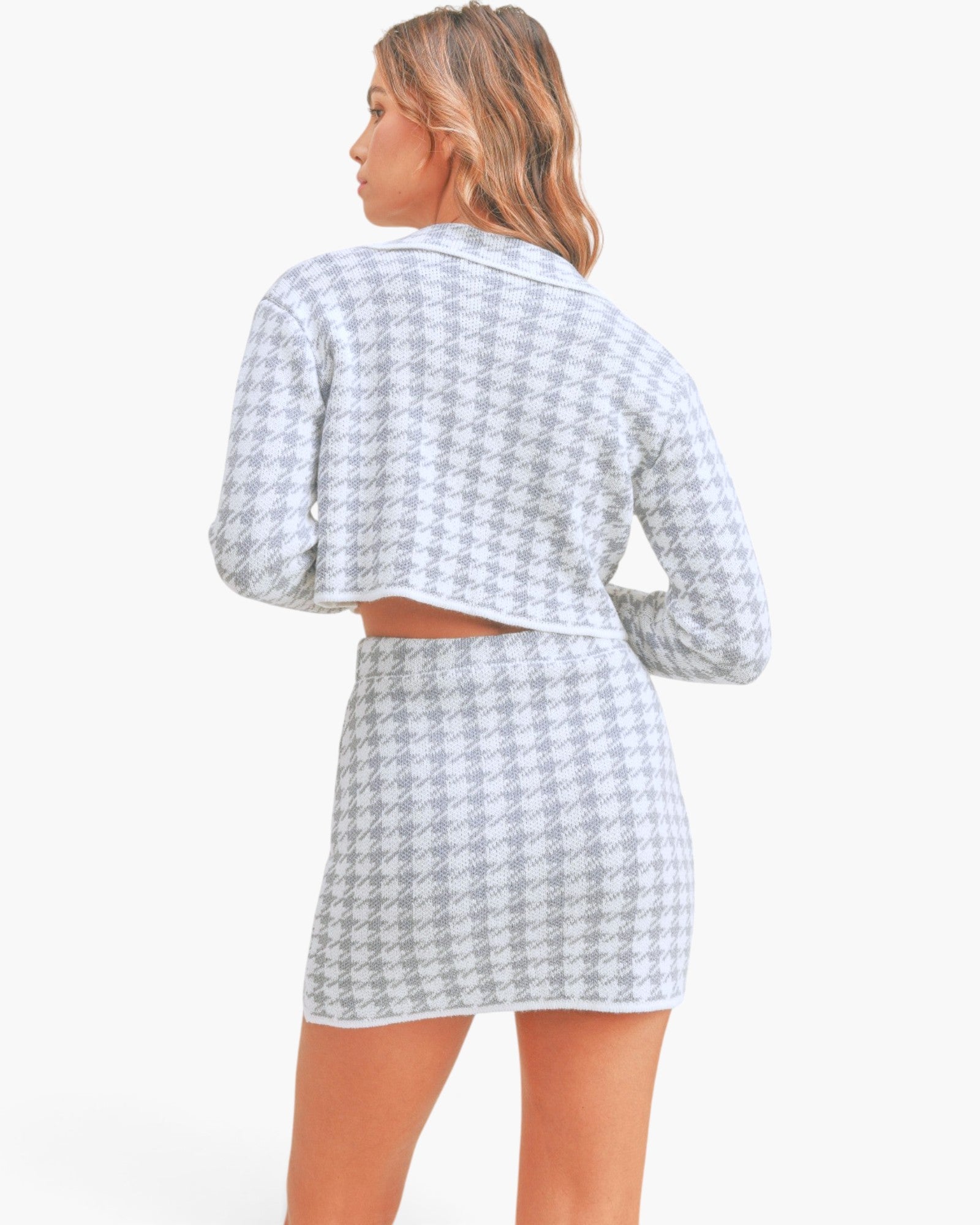 A woman shown from the back wearing a matching long-sleeve cropped cardigan and mini skirt set in a light gray and white houndstooth pattern, against a plain white studio background.