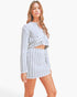 A woman modeling a matching two-piece outfit featuring a light gray and white houndstooth pattern, consisting of a long-sleeve cropped top and a high-waisted mini skirt, against a plain white studio background.