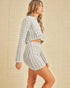 Woman wearing a checkered outfit against a beige tiled wall