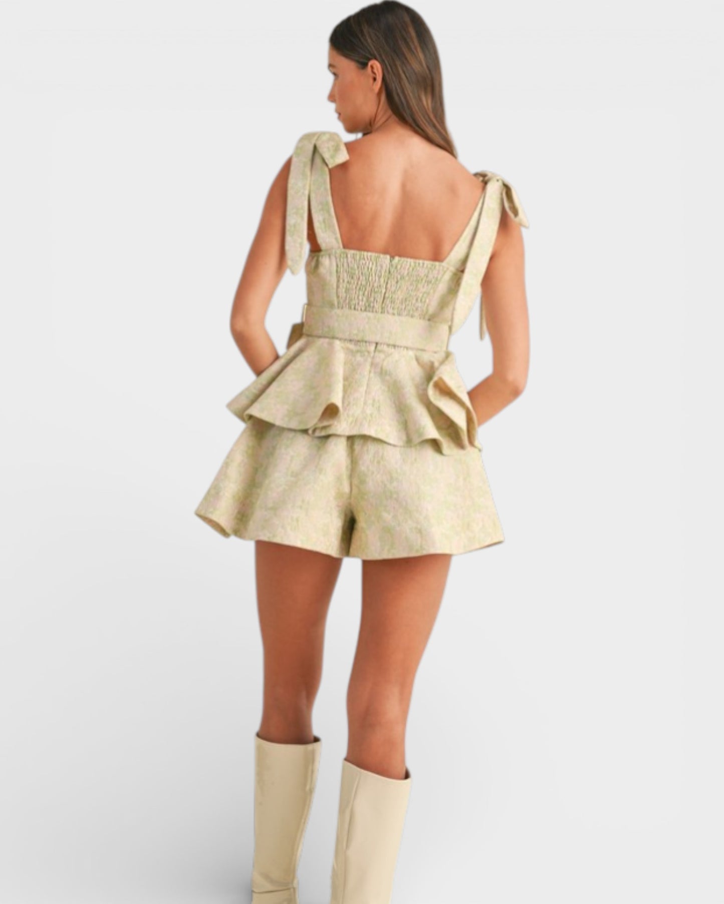 Woman wearing a beige peplum top and shorts with matching knee-high boots on a white background