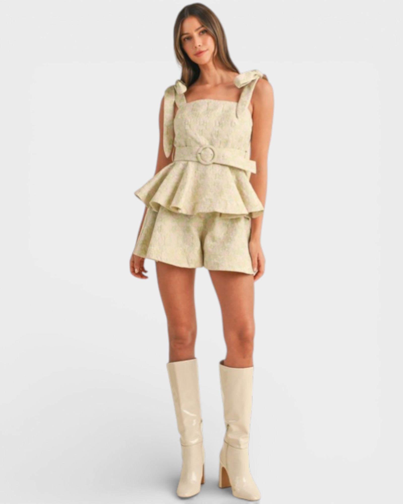 Woman wearing a beige peplum top and shorts with matching boots on a white background