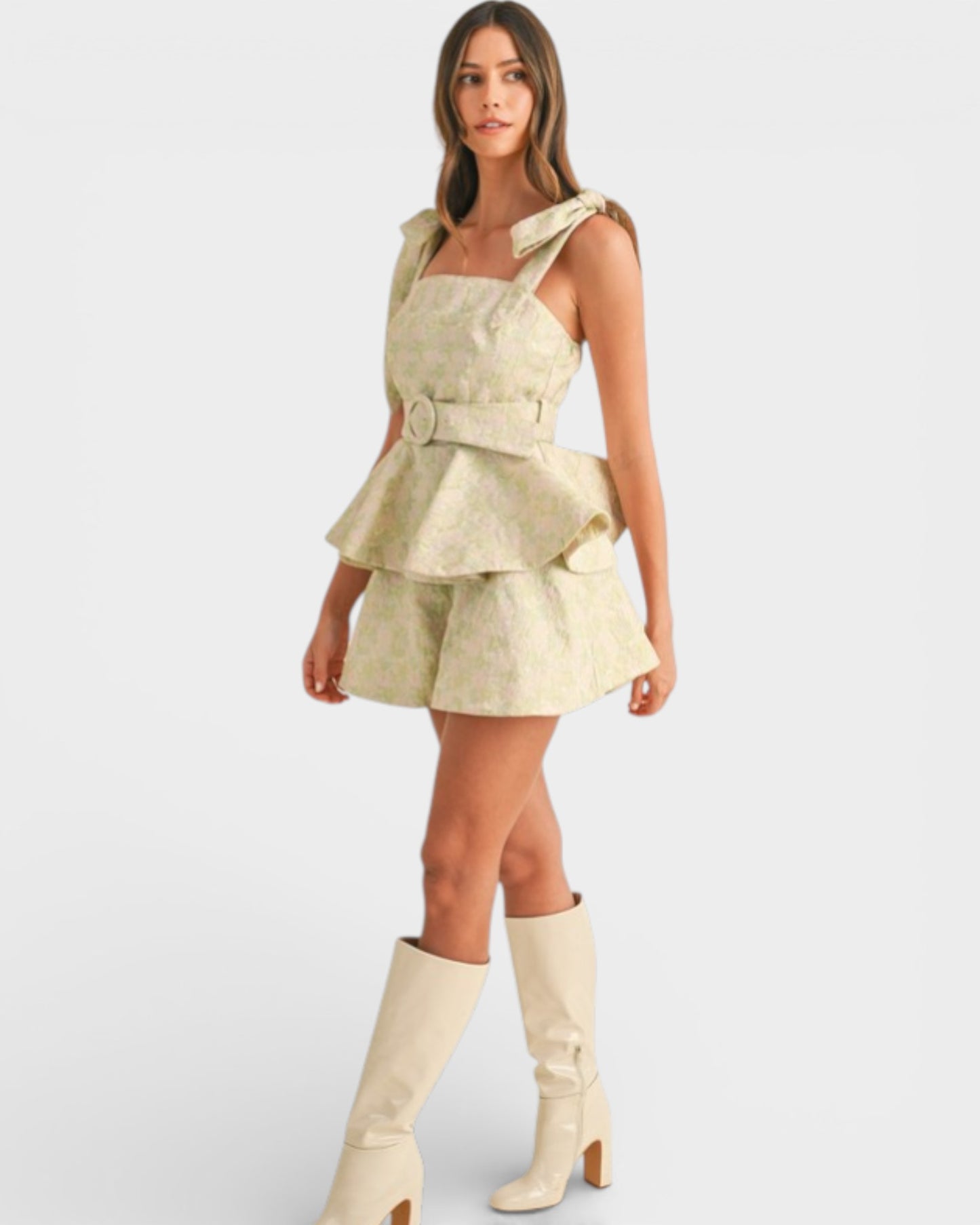 Woman wearing a beige dress with ruffled layers and matching knee-high boots on a white background