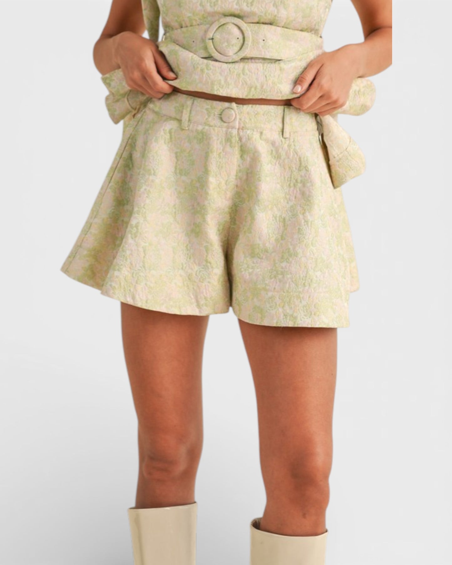 Person wearing a light-colored outfit with shorts and a belt on a white background