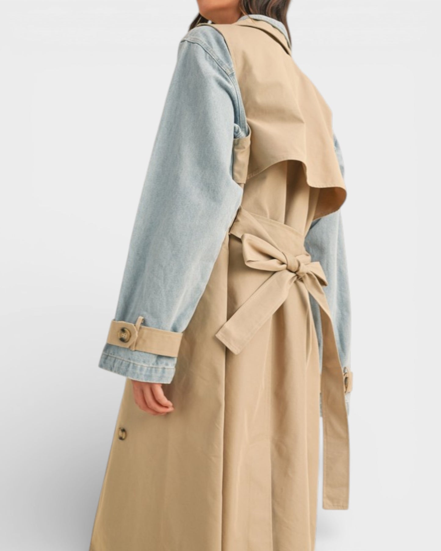 Person wearing a beige trench coat with denim sleeves on a white background
