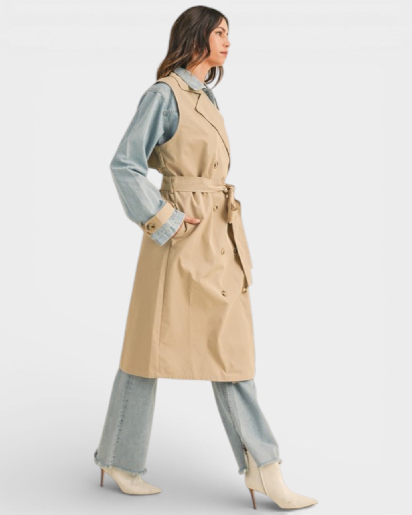 Woman wearing a beige trench coat over a denim outfit on a white background