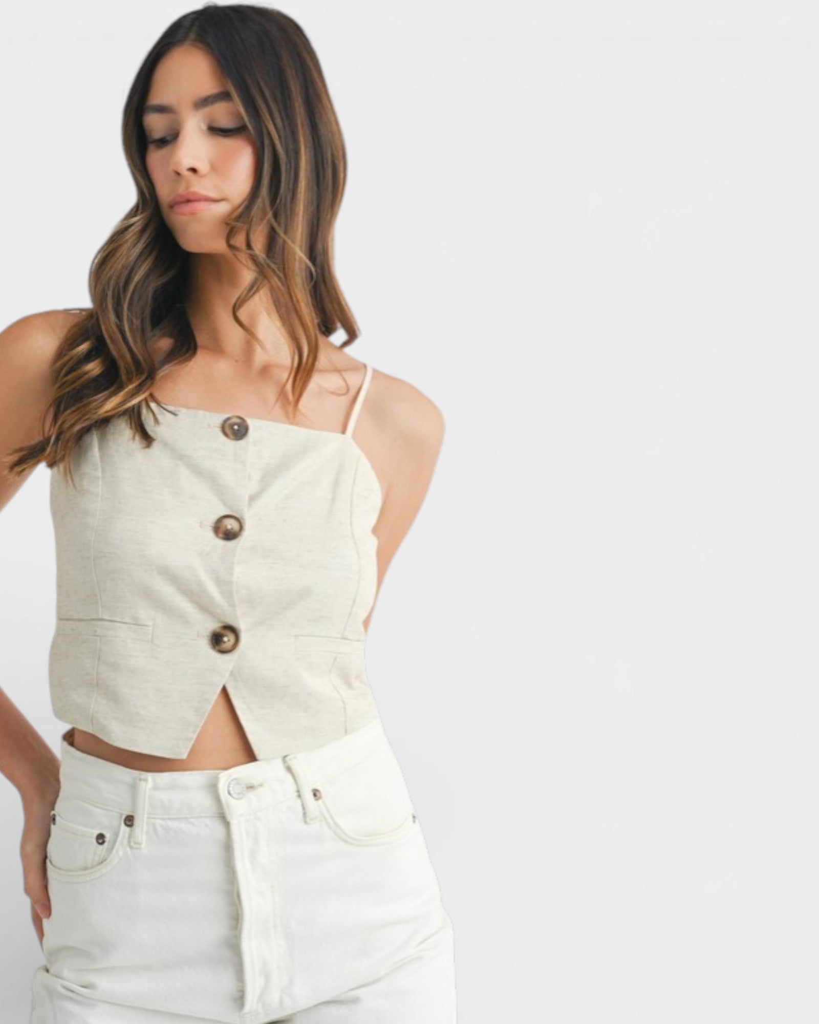 Woman wearing a beige button-up top and white pants on a plain background