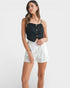 Woman wearing a black top with button details and white shorts on a white background