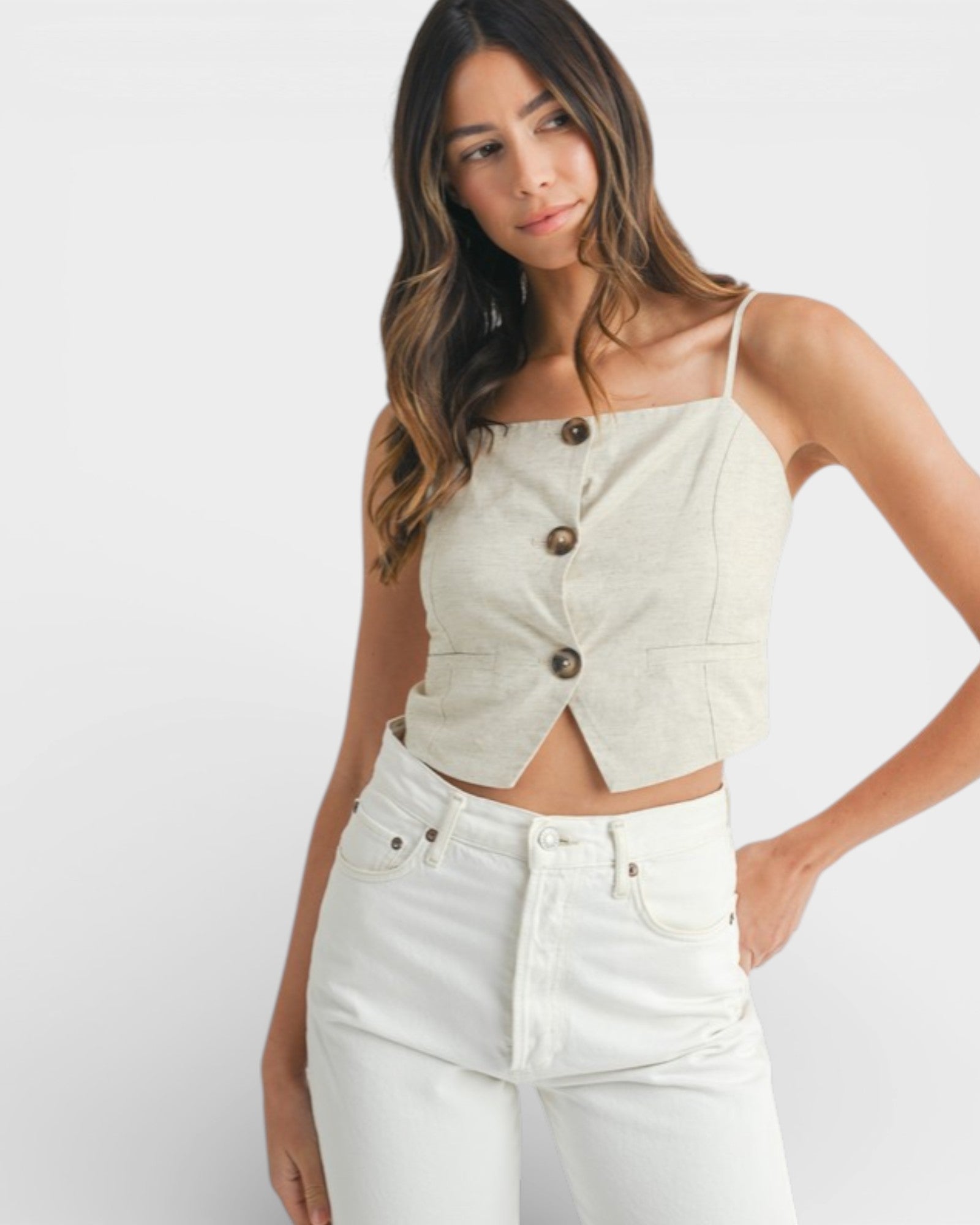 Woman wearing a light-colored button-up top and white pants on a plain background