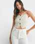 Woman wearing a light-colored button-up top and white pants on a plain background