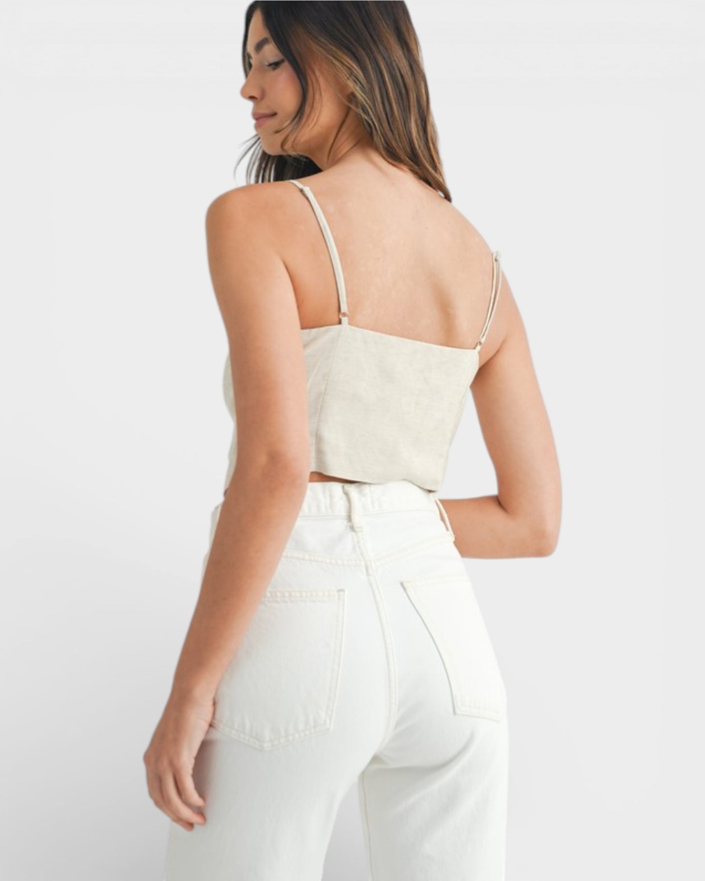 Woman wearing a beige crop top and white pants on a plain background