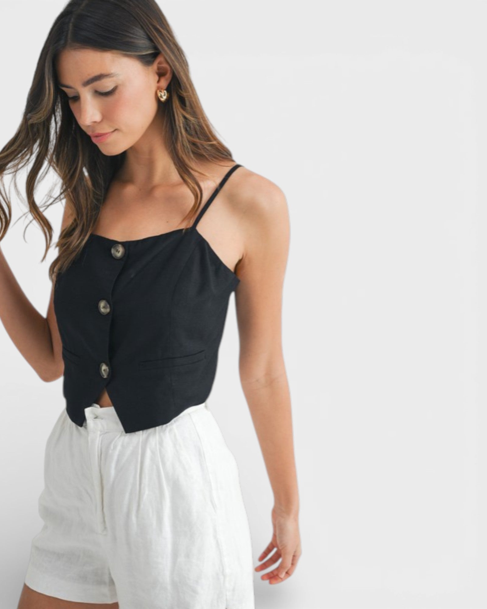 Woman wearing a black top with thin straps and white shorts on a plain background