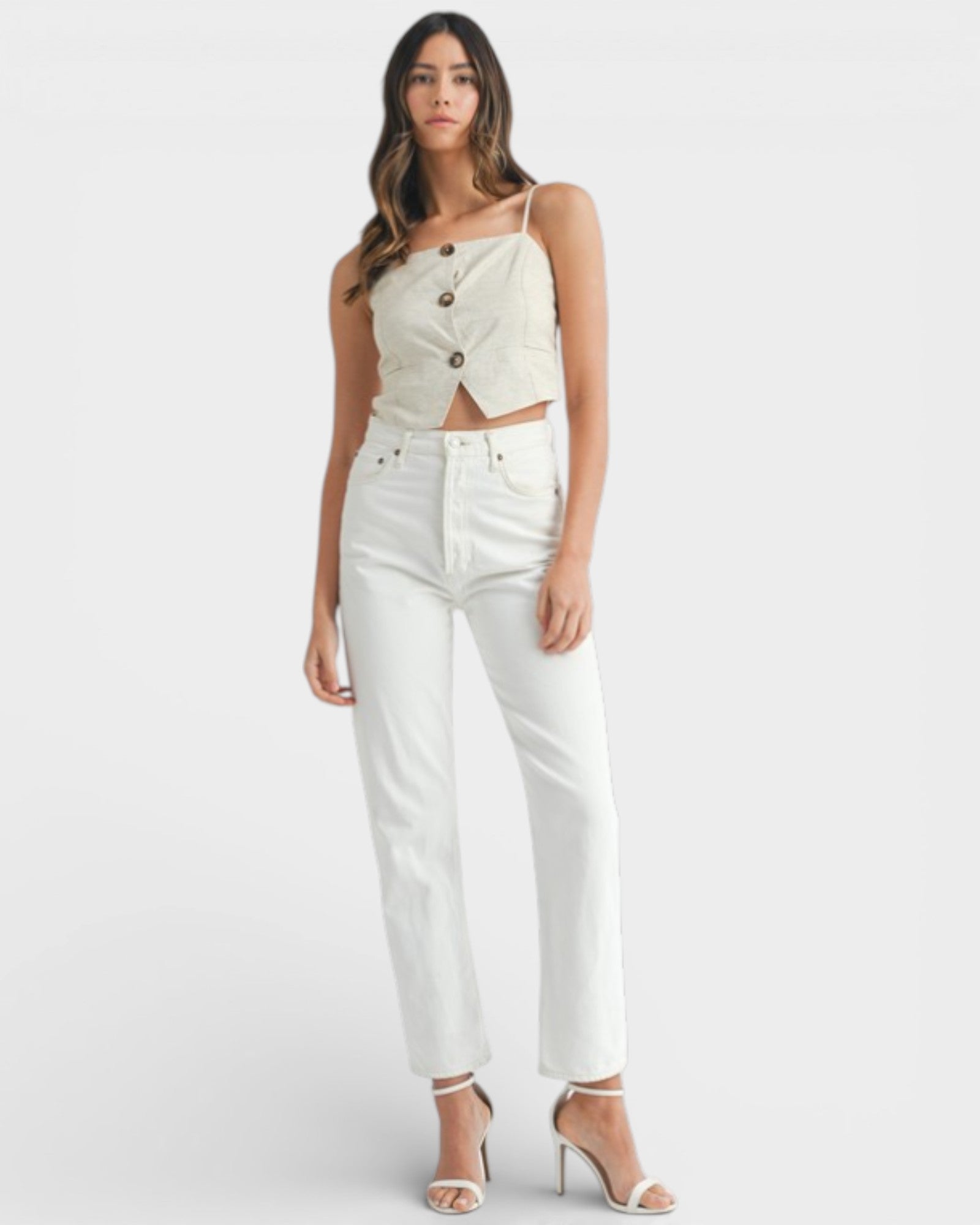 Woman wearing a white sleeveless top with button details and white pants on a light gray background