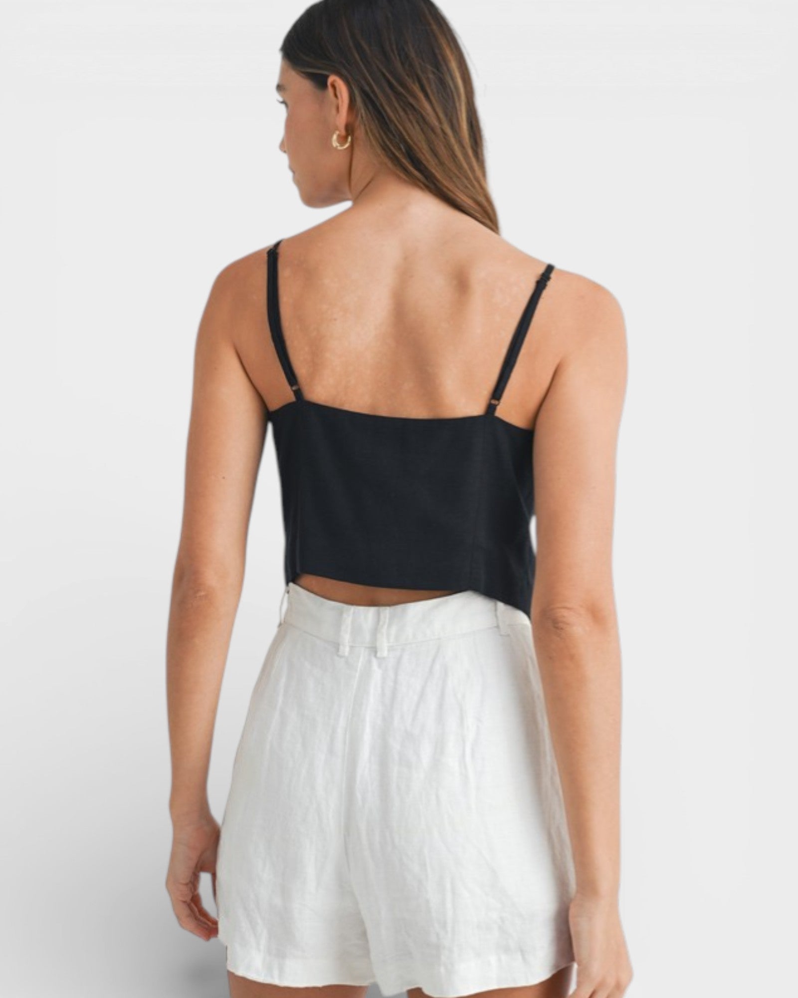 Woman wearing a black top and white shorts on a plain background