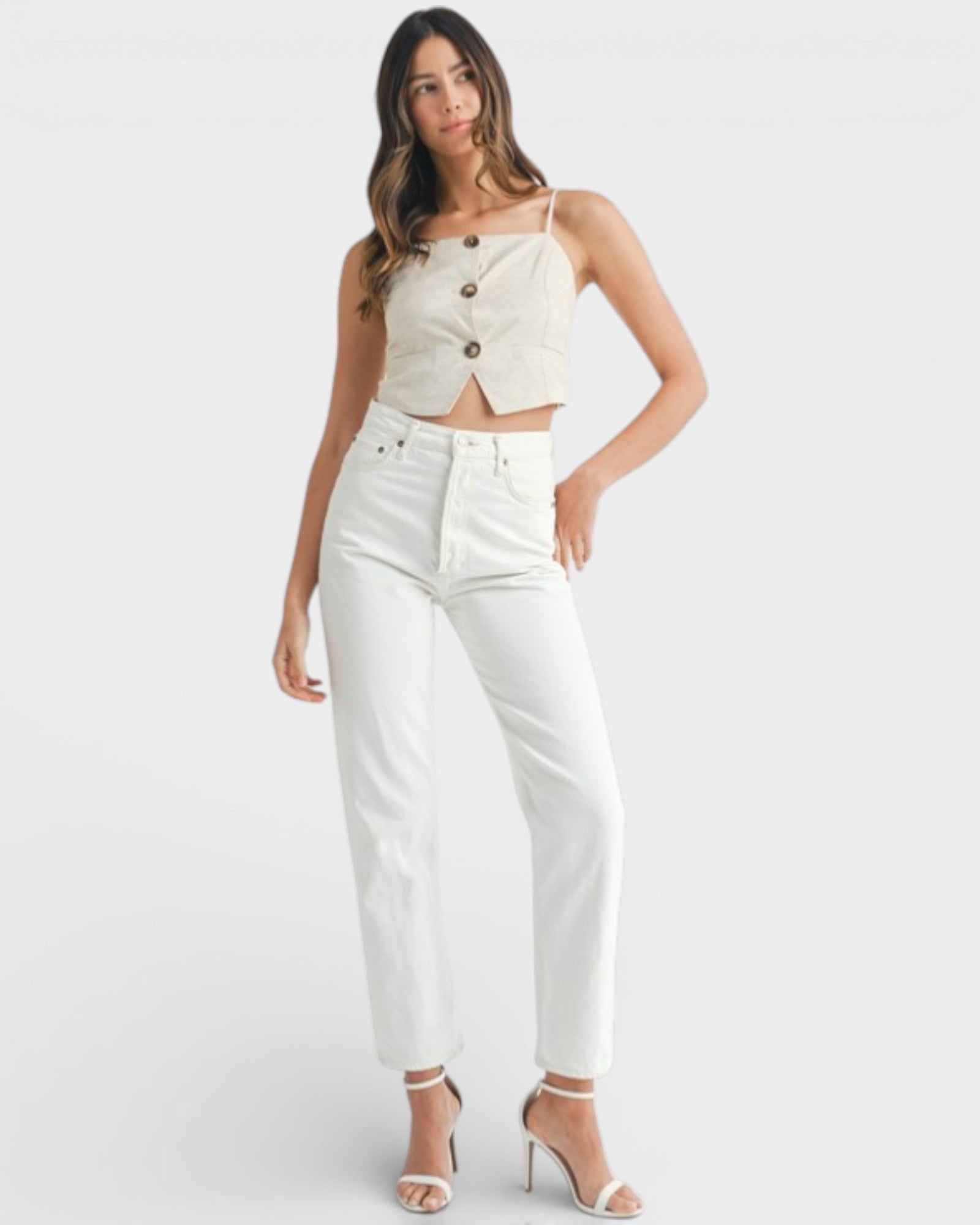 Woman wearing a white crop top with buttons and high-waisted white pants on a light gray background