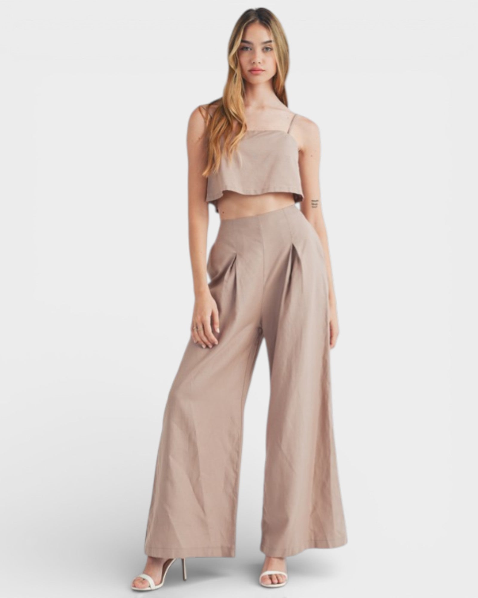 Woman wearing a beige sleeveless top and wide-leg pants on a white background