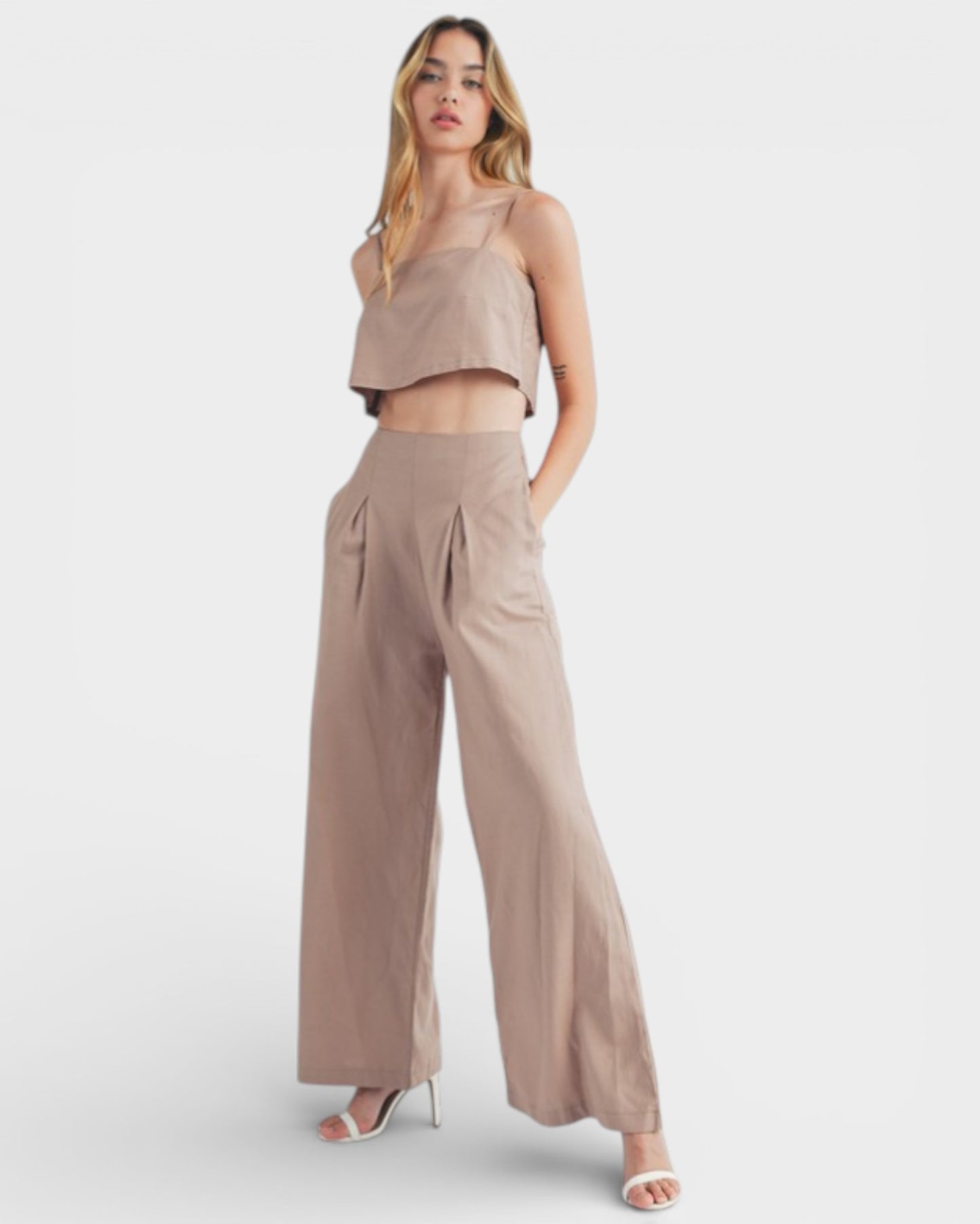 Woman wearing a beige sleeveless top and wide-leg pants on a white background