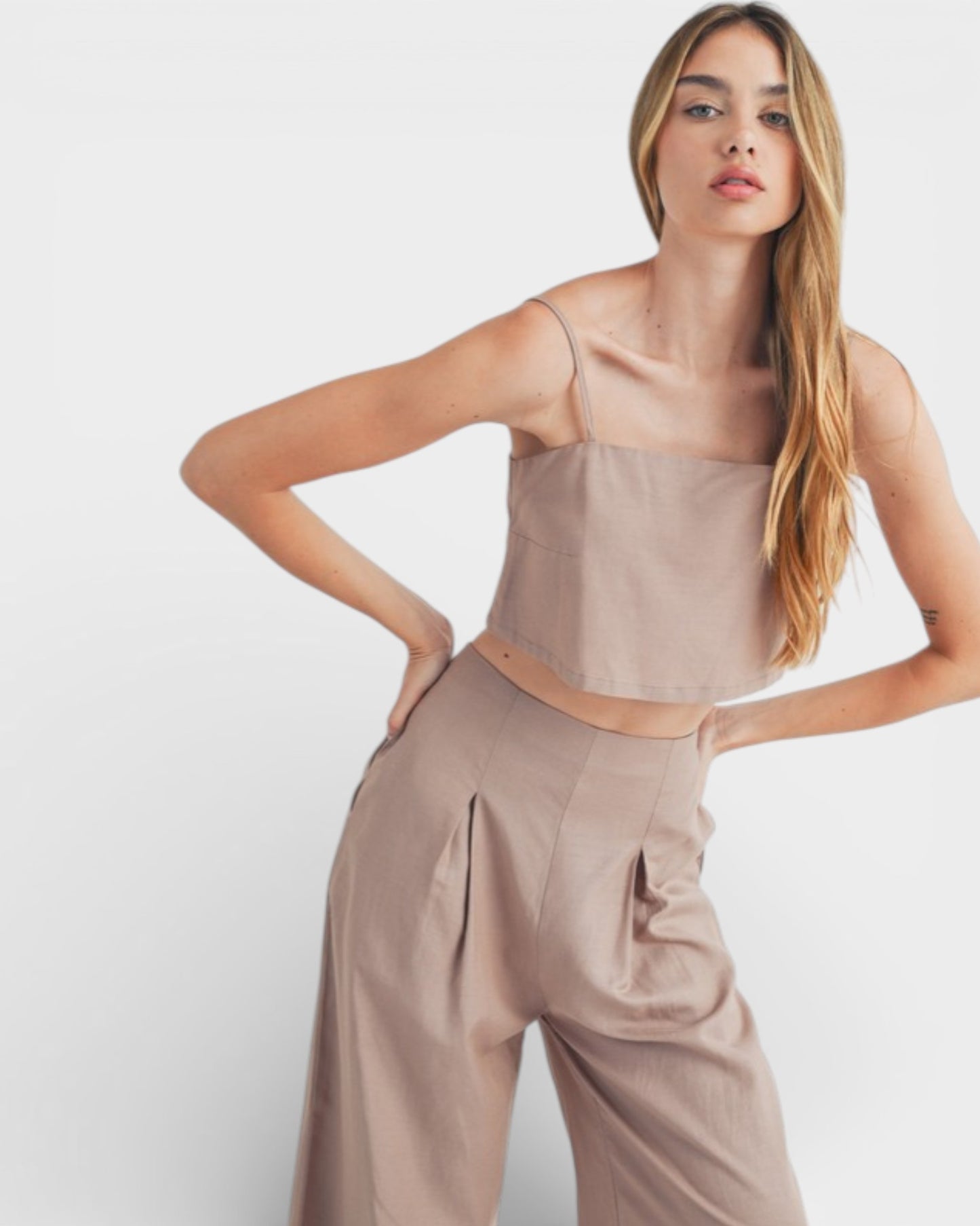 Woman wearing a beige top and pants against a white background