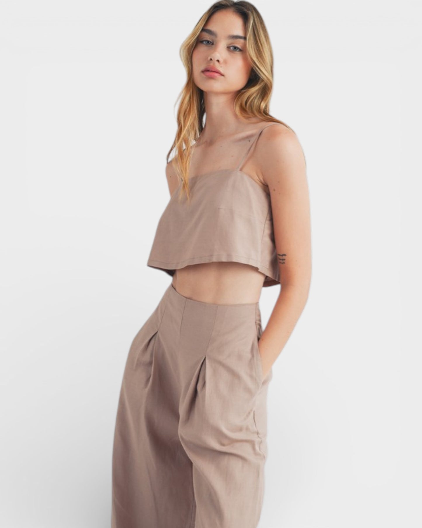 Woman wearing a beige sleeveless top and high-waisted pants on a white background