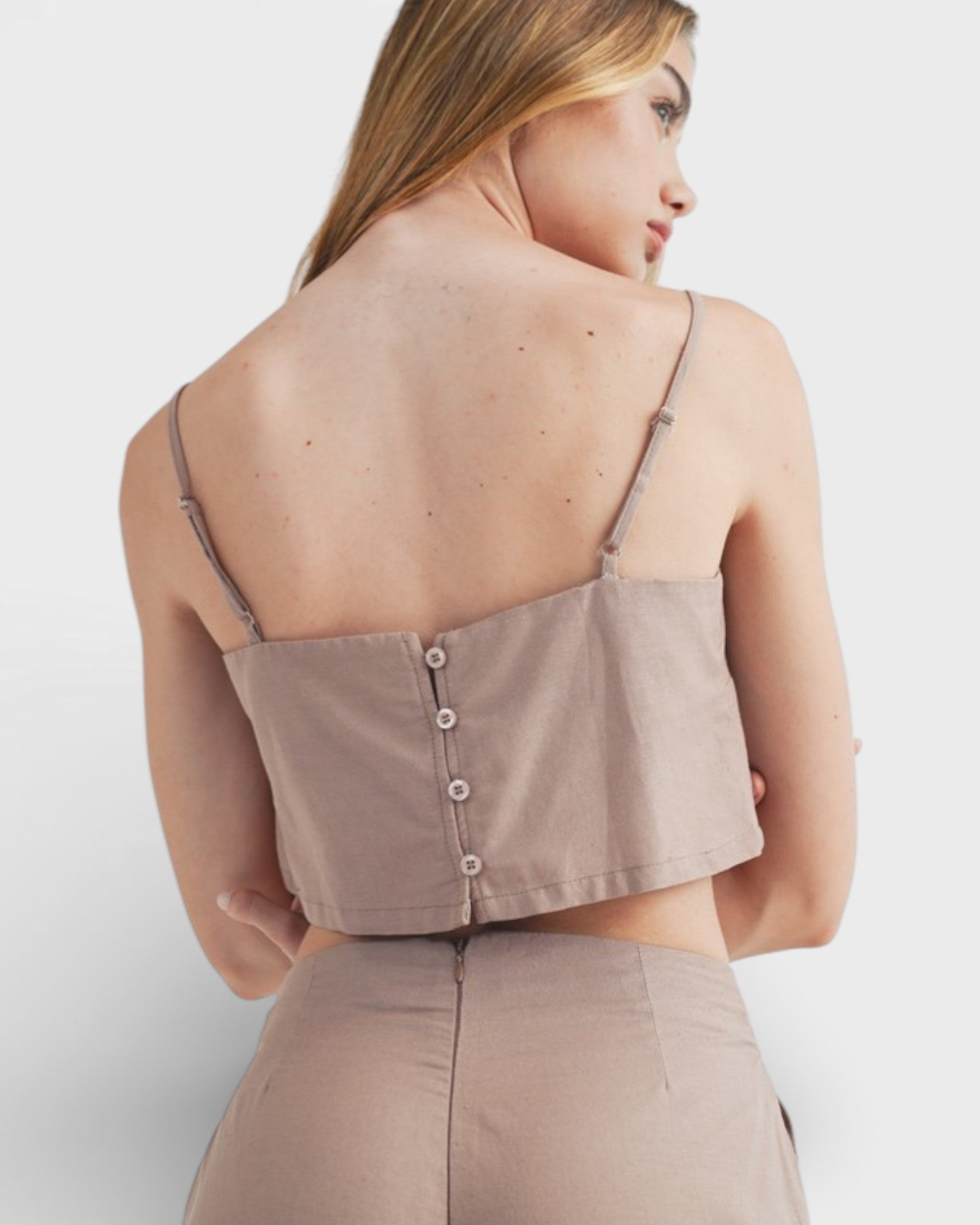 Woman wearing a beige button-up top with thin straps on a white background