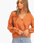 A woman wearing a fuzzy orange cardigan sweater with button details on the front and cuffs, paired with light blue jeans, against a plain white background.