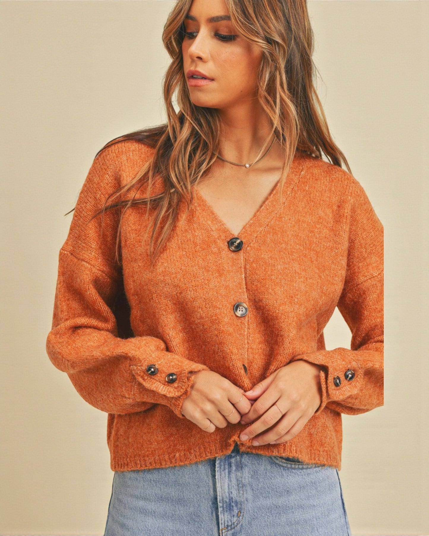Woman wearing an orange sweater with black buttons against a beige background