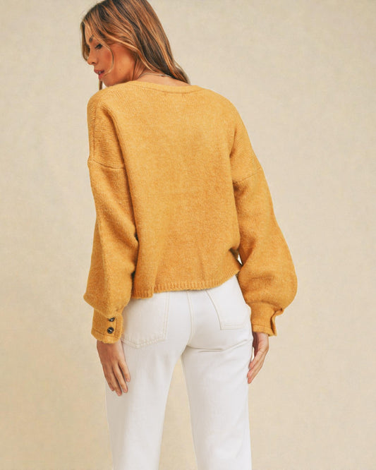 Woman wearing a mustard yellow sweater and white pants against a beige background