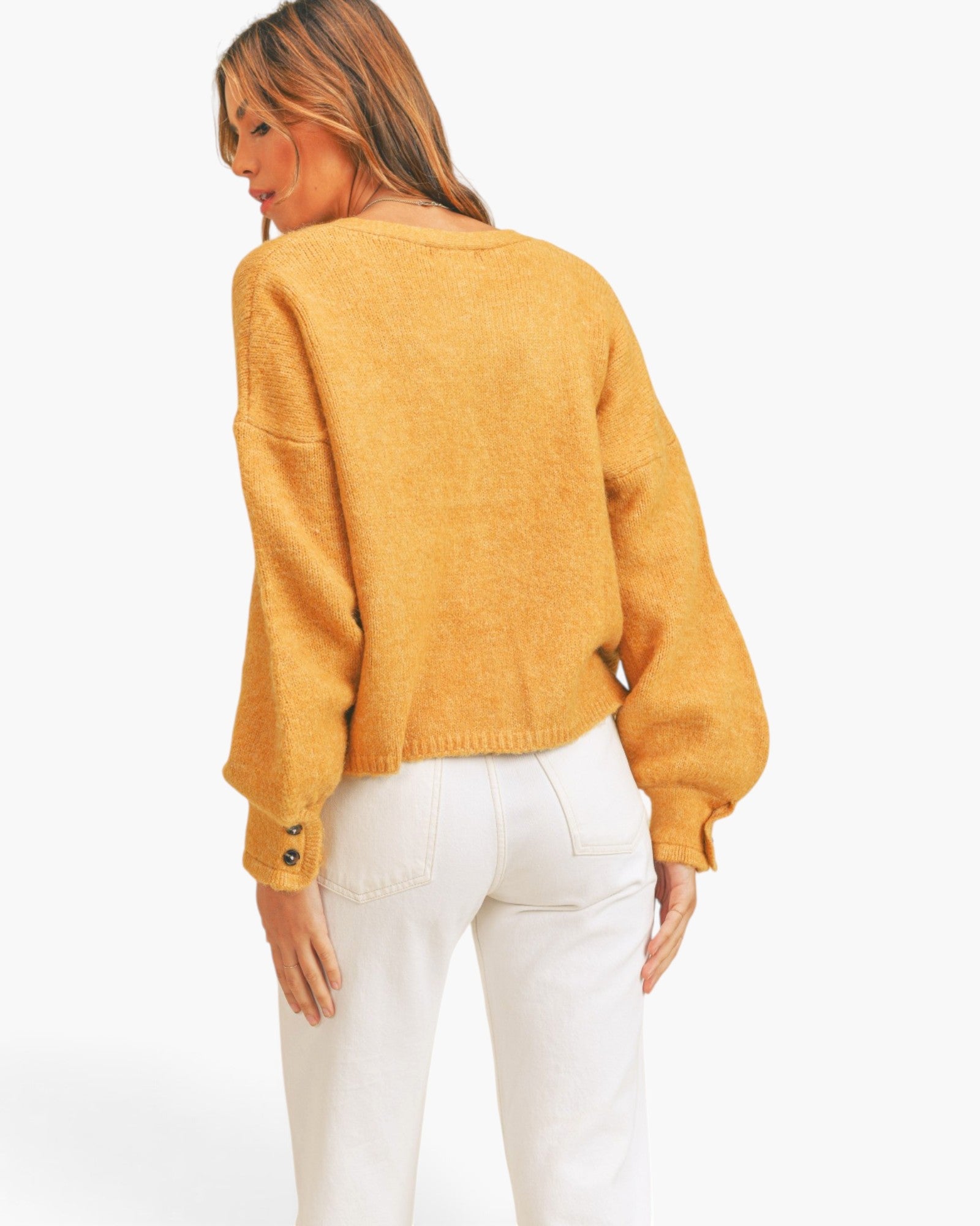 A woman shown from the back wearing a fuzzy mustard yellow cropped sweater with balloon sleeves and white pants, against a plain white studio background.