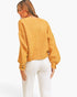 A woman shown from the back wearing a fuzzy mustard yellow cropped sweater with balloon sleeves and white pants, against a plain white studio background.
