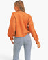 A woman shown from the back wearing a fuzzy orange cropped sweater and light blue jeans against a plain white studio background.
