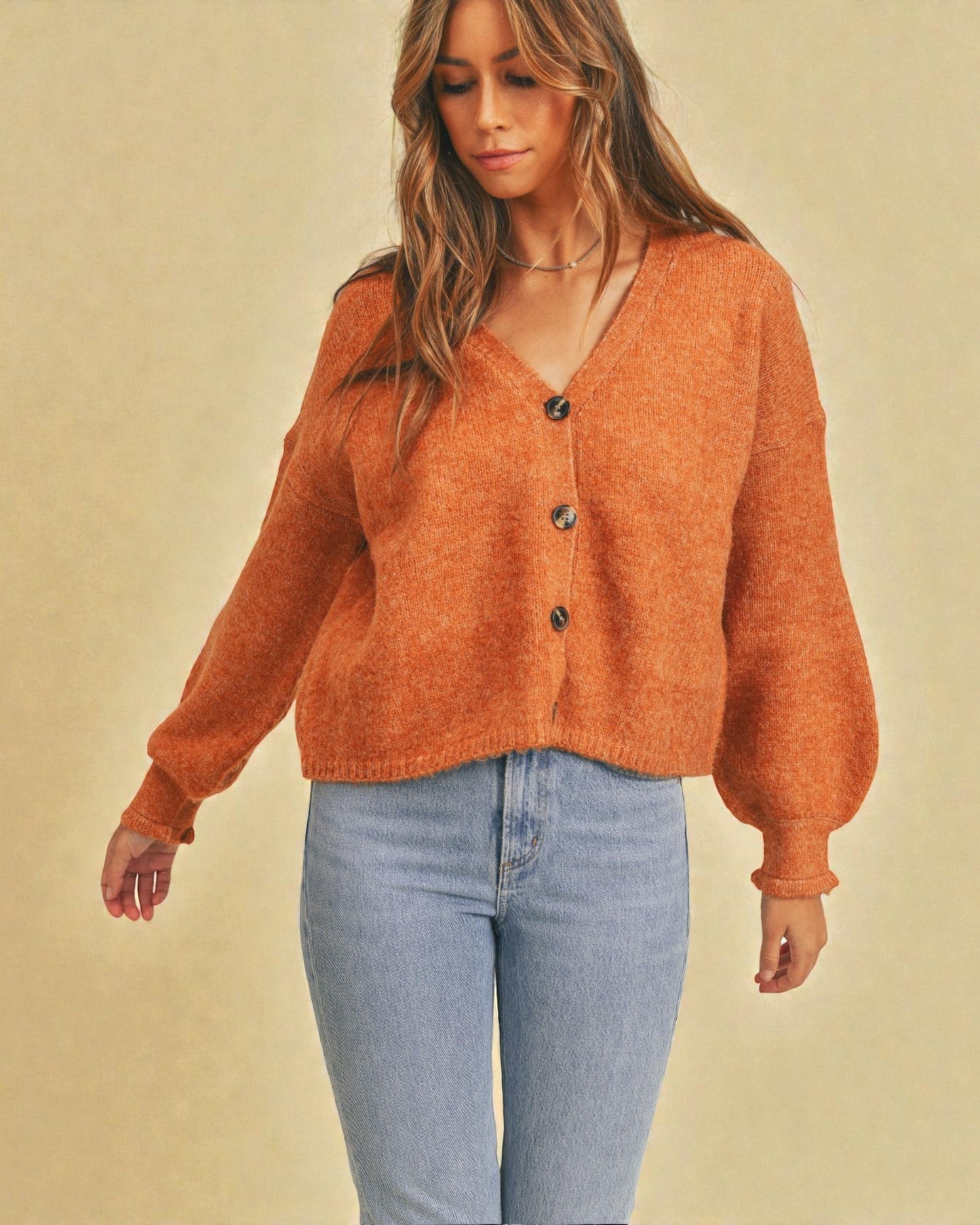 Woman wearing an orange sweater with black buttons against a beige background