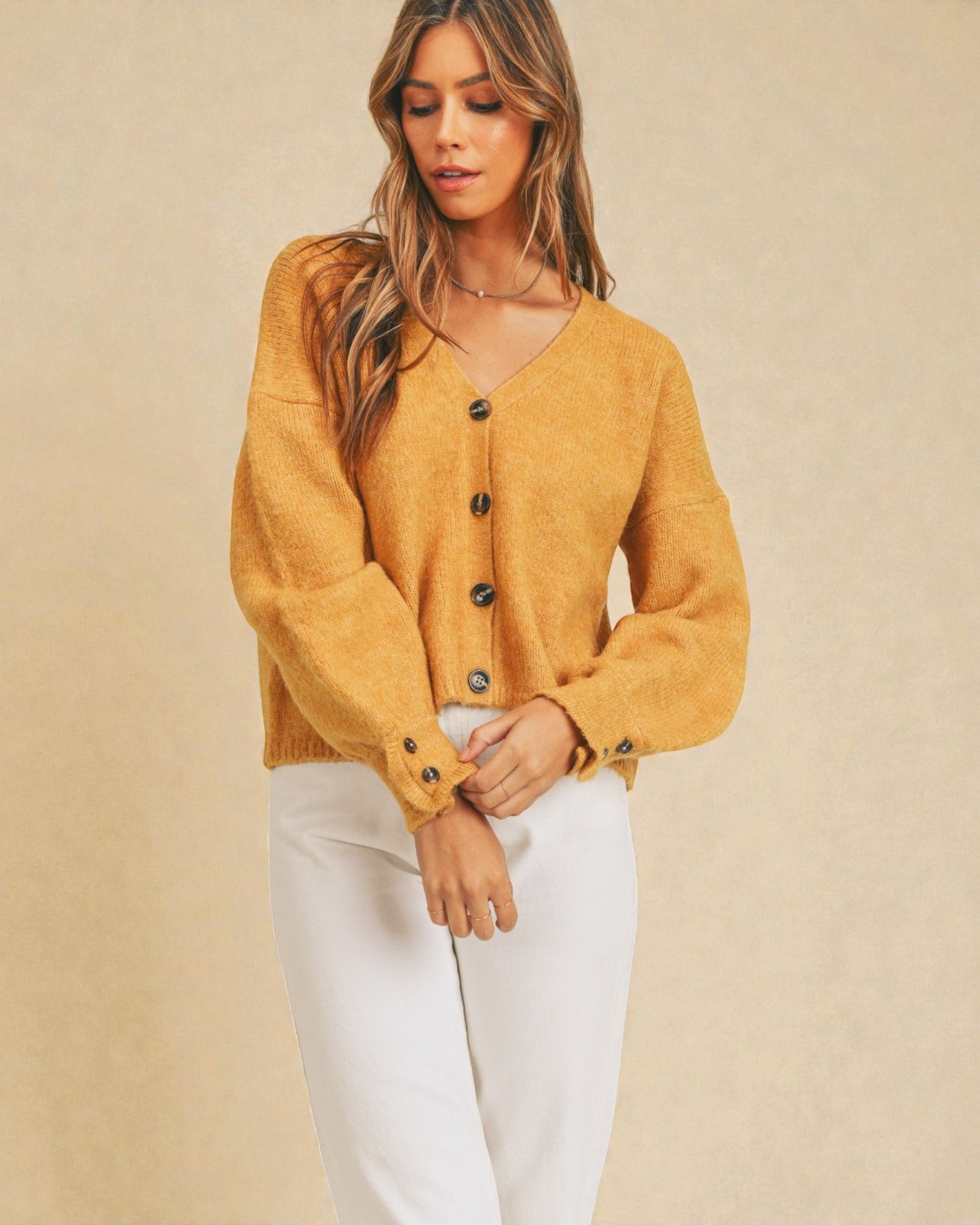 Woman wearing a mustard yellow cardigan over a white top against a beige background
