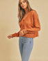 Woman wearing a rust-colored sweater and light blue jeans against a beige background