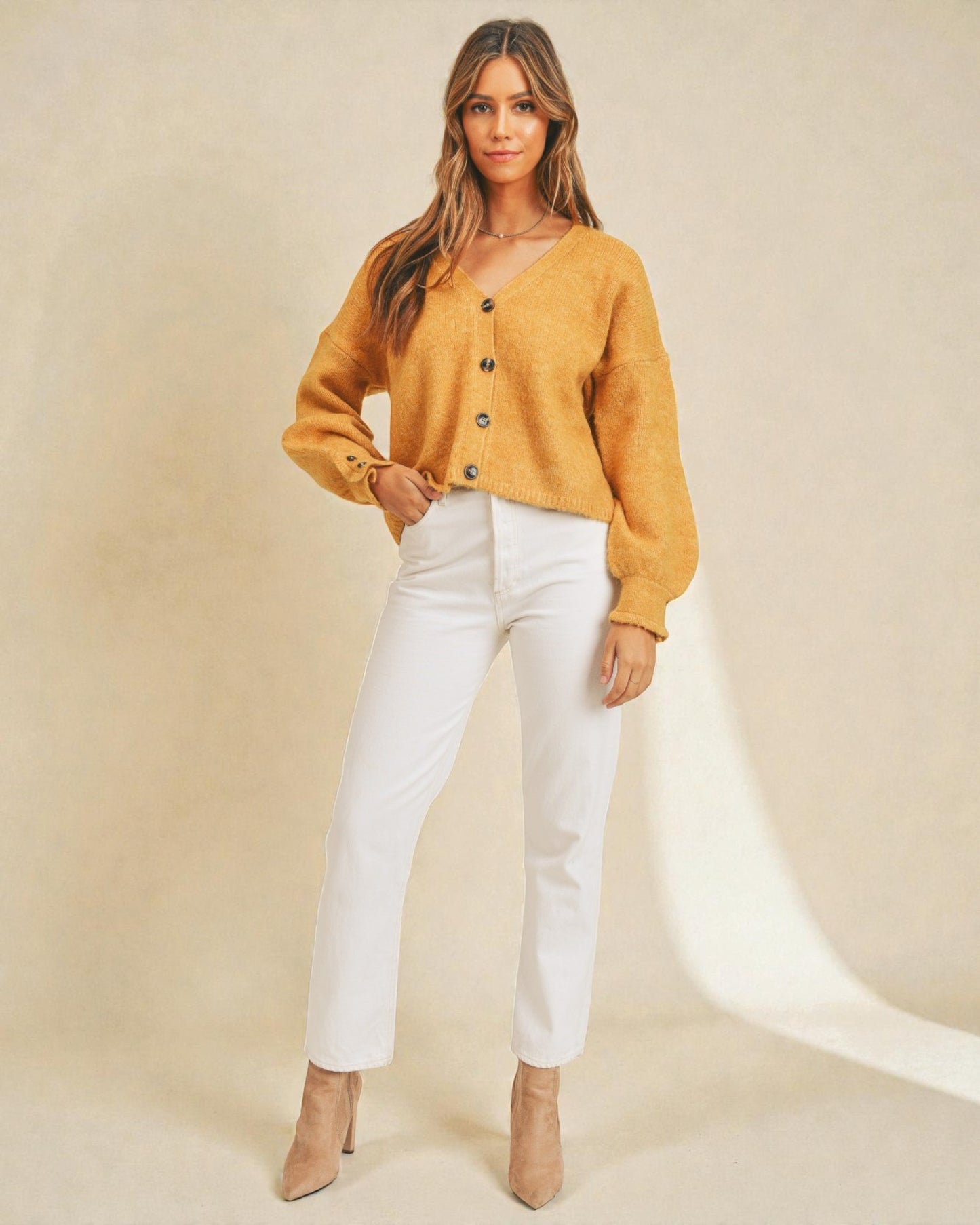Woman wearing a mustard yellow sweater and white pants on a beige background