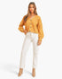 A woman modeling a fuzzy mustard yellow cardigan with white pants and beige ankle boots, standing against a light gray studio background.