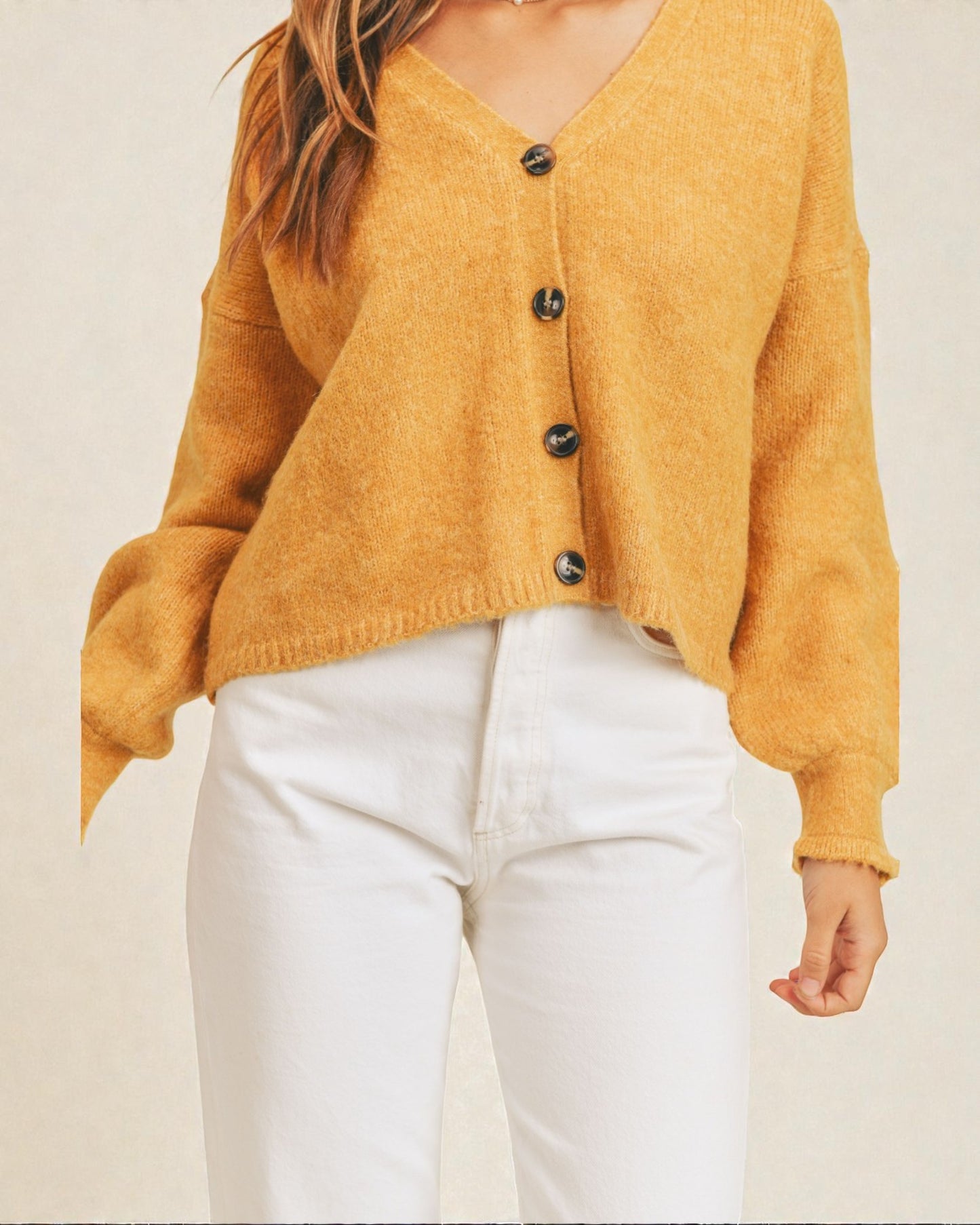 Mustard yellow cardigan worn by a person on a beige background