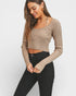 Woman wearing a beige ribbed long-sleeve top and black pants on a white background