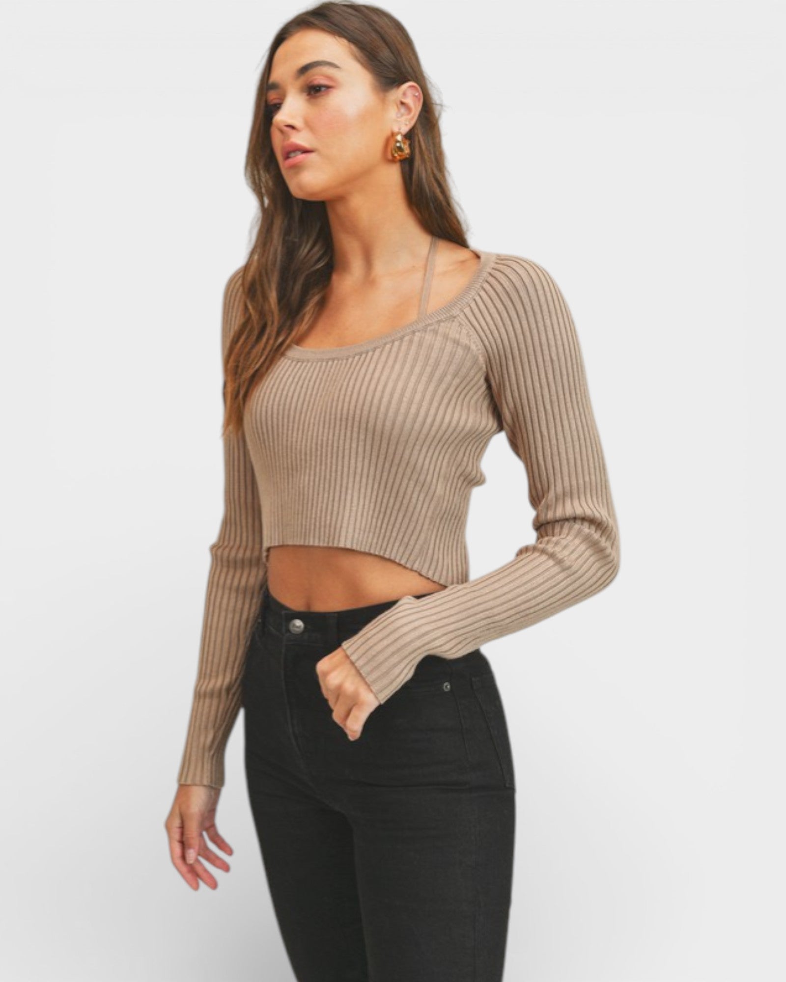 Woman wearing a beige ribbed long-sleeve top and black pants on a white background