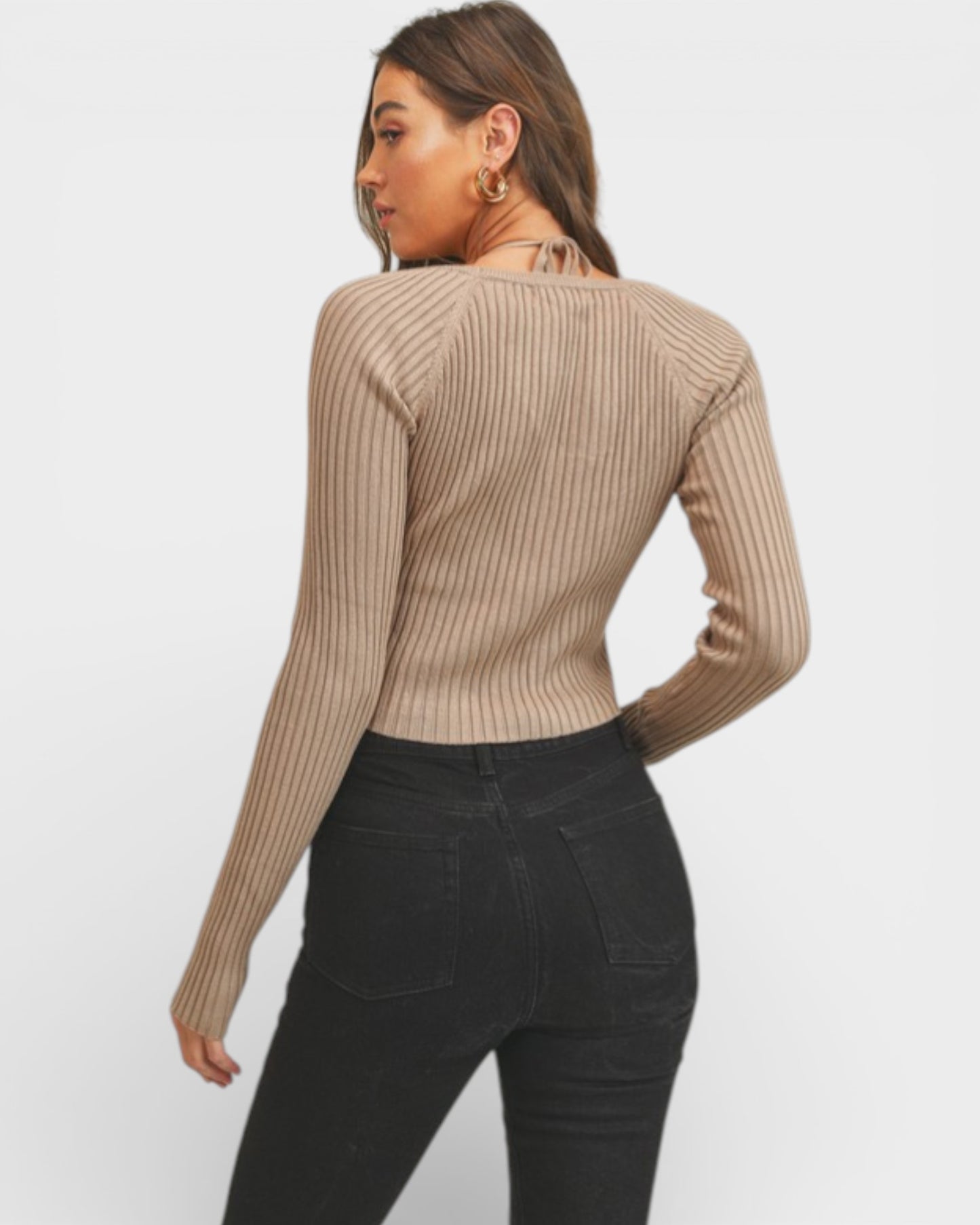 Woman wearing a beige ribbed sweater and black pants on a white background