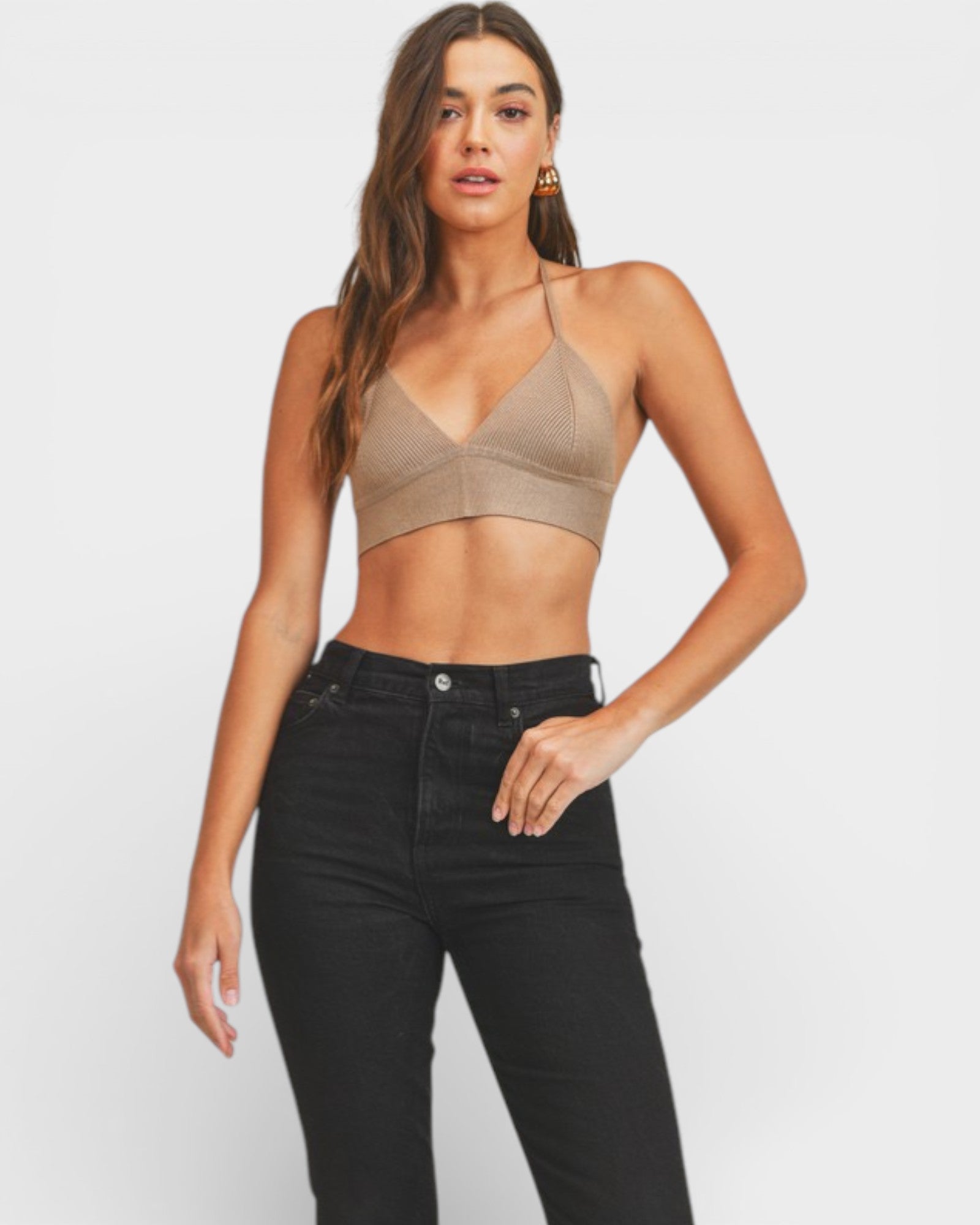 Woman wearing a brown bralette and black jeans on a white background